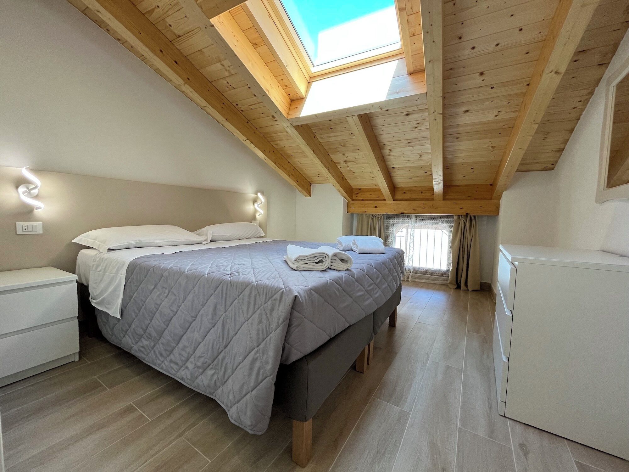 Un dormitorio con cama, mesitas de noche, armario y tragaluz.