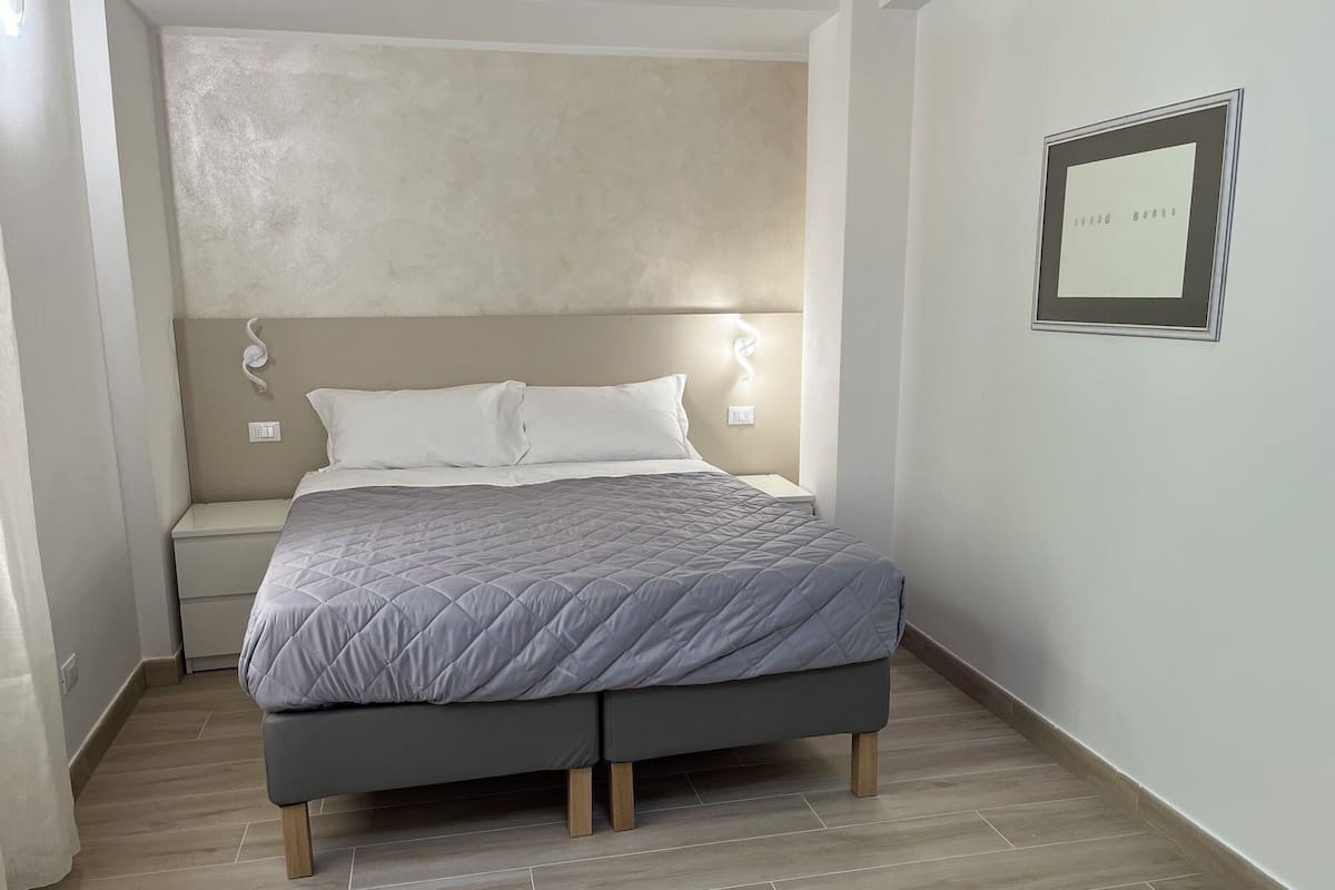 Ein Schlafzimmer mit einem Bett, Nachttischen, einer Wandleuchte und einem gerahmten Bild.