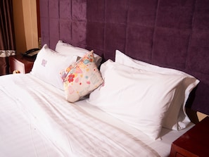 A bed with white linens, a purple headboard, and a decorative pillow with floral patterns.