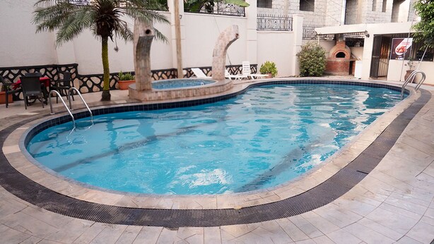 Una piscina con borde de azulejos, una palmera y un horno de ladrillo al fondo.
