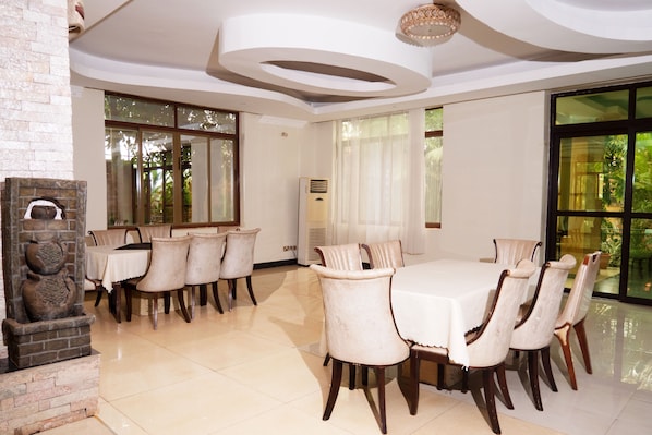 A dining area with a round table, chairs, a stone fireplace, and large windows.