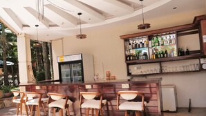 Una zona de bar con taburetes de madera, un refrigerador y una estantería con botellas.