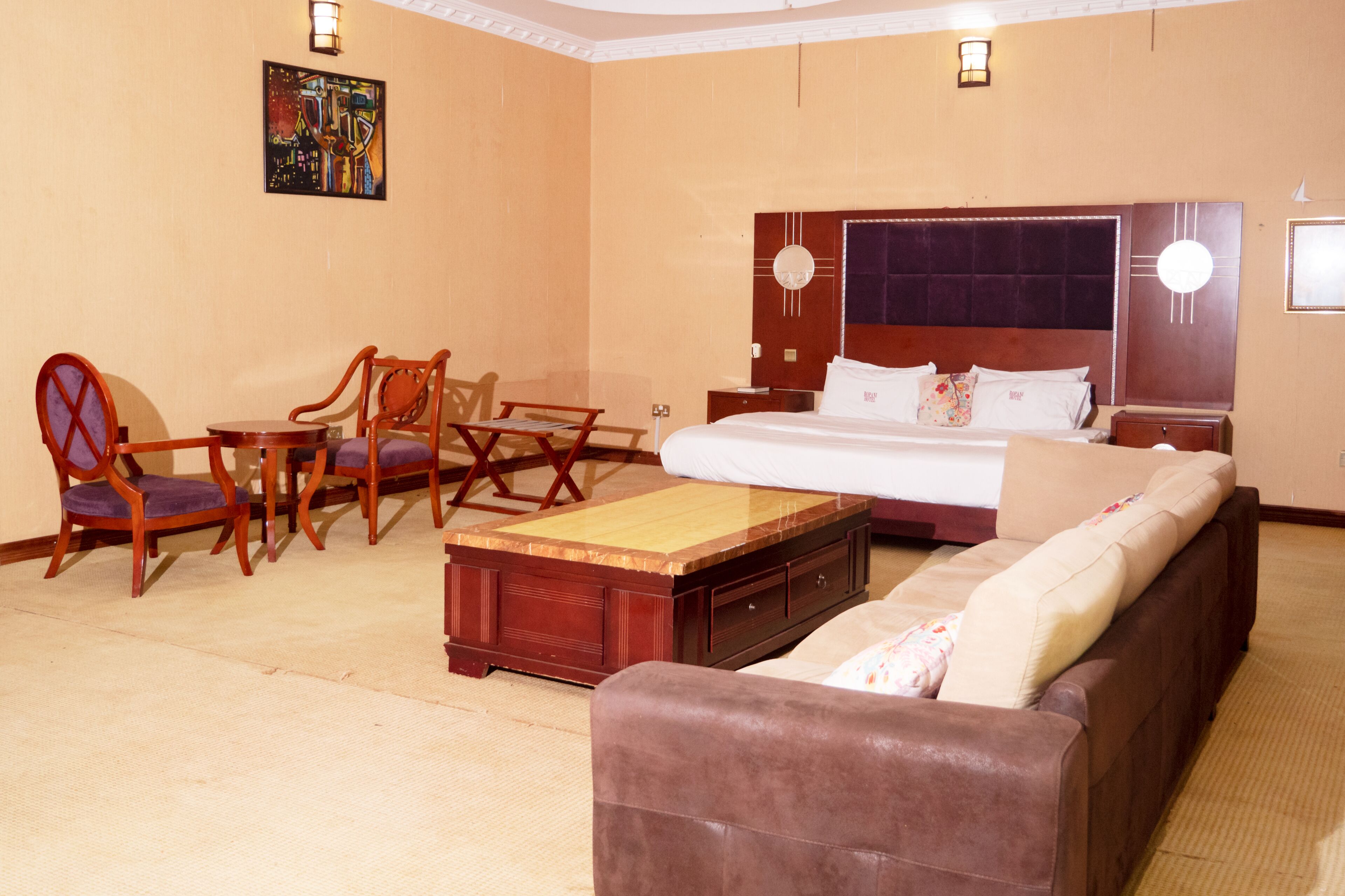 A hotel room with a bed, a sofa, a wooden coffee table, and two chairs.