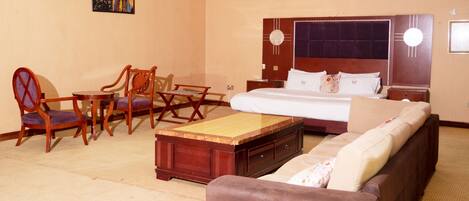 A hotel room with a bed, a sofa, a wooden coffee table, and two chairs.