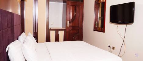 A hotel room with a bed, a bedside telephone, a television mounted on the wall, and a door with a mirror.