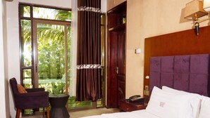 Habitación de hotel con cama, una silla, un escritorio con teléfono y una ventana con cortinas.
