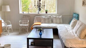 A cozy living room with a sofa, a coffee table, a chair, and a window with a view of trees. - 6 Person Holiday Home in Mellbystrand (Mellbystrand)