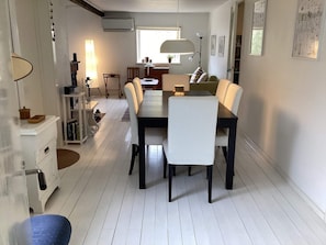 A dining area with a long table, white chairs, a lamp, and a bookshelf. - 6 Person Holiday Home in Mellbystrand (Mellbystrand)