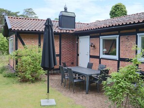 Ein Ziegelhaus mit Ziegeldach, eine Terrasse mit Tisch und Stühlen sowie ein schwarzer Sonnenschirm.