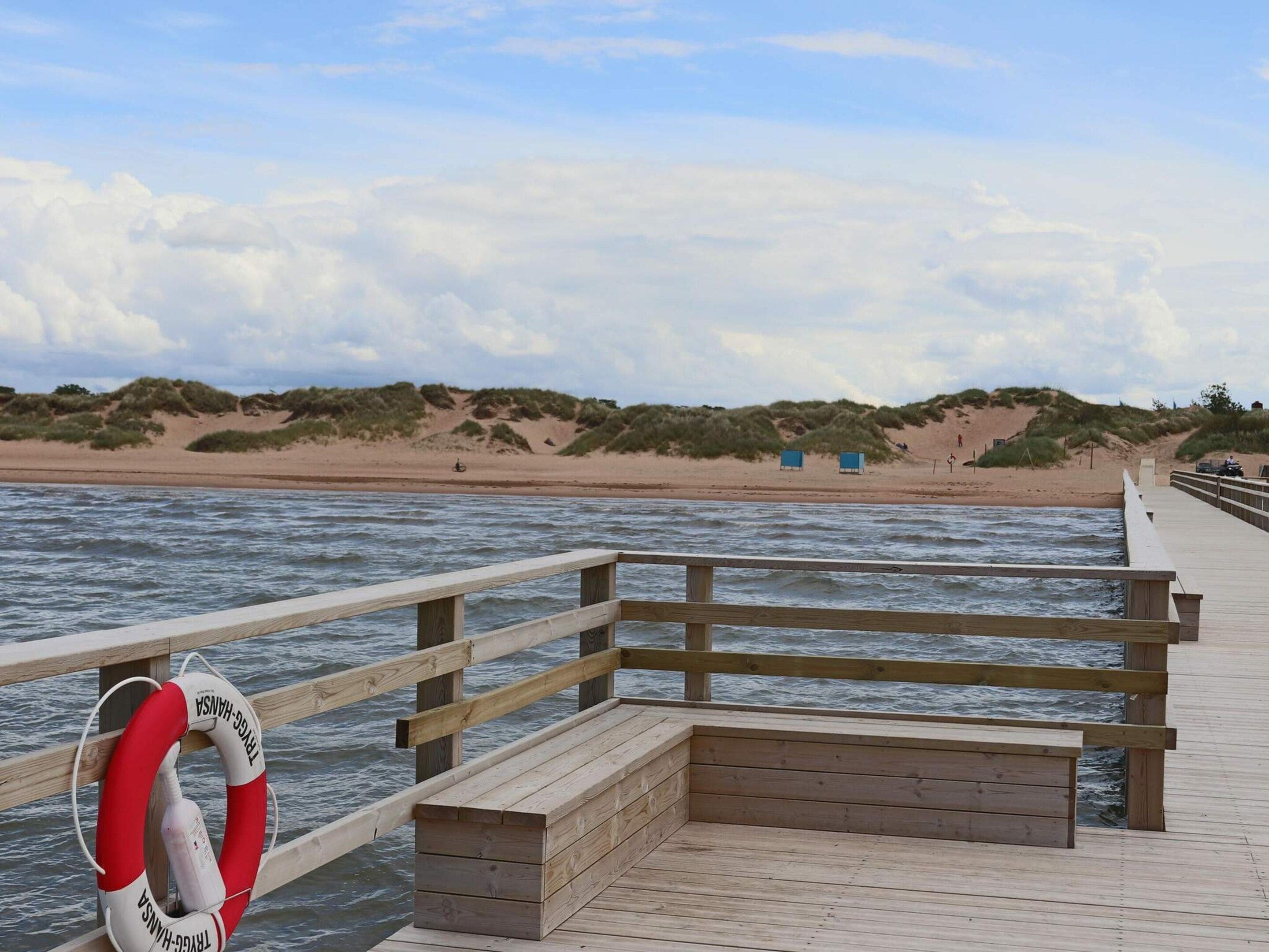 A wooden pier extending into calm waters with a lifebuoy attached to the railing.