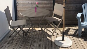 A patio with a round table, two chairs, a large umbrella, and a wooden fence. - Very comfortable single-storey house 2 minutes from the ocean on the island of Noirmoutier (L'EPINE)