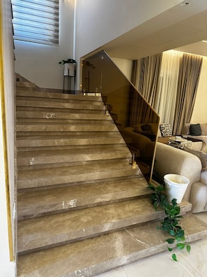 Eine Treppe mit Glastrennwand führt zu einem Wohnbereich mit Sofa und Pflanze.