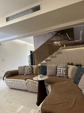 Ein modernes Wohnzimmer mit einem Ecksofa, einem runden Couchtisch und einer Treppe mit Geländer.