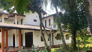 A two-story building with a covered patio, outdoor seating, and lush greenery. - GB Royal Stay Nuwara Wewa (Anuradhapuraya)