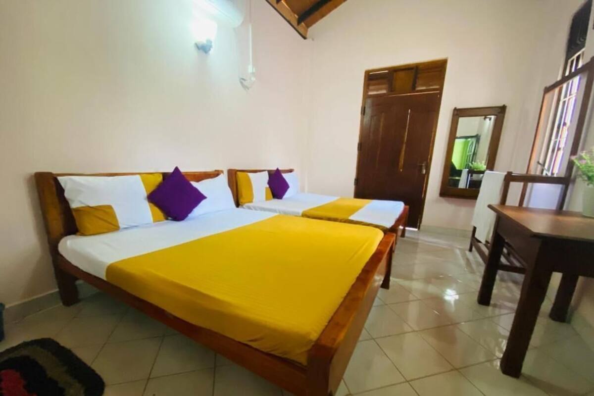A double bed with a yellow bedspread, a wooden headboard, and multiple pillows in white, yellow, and purple.