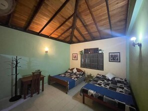 A room with two beds, a dining table, a coat rack, and a ceiling with wooden beams. - GB Royal Stay Nuwara Wewa (Anuradhapuraya)