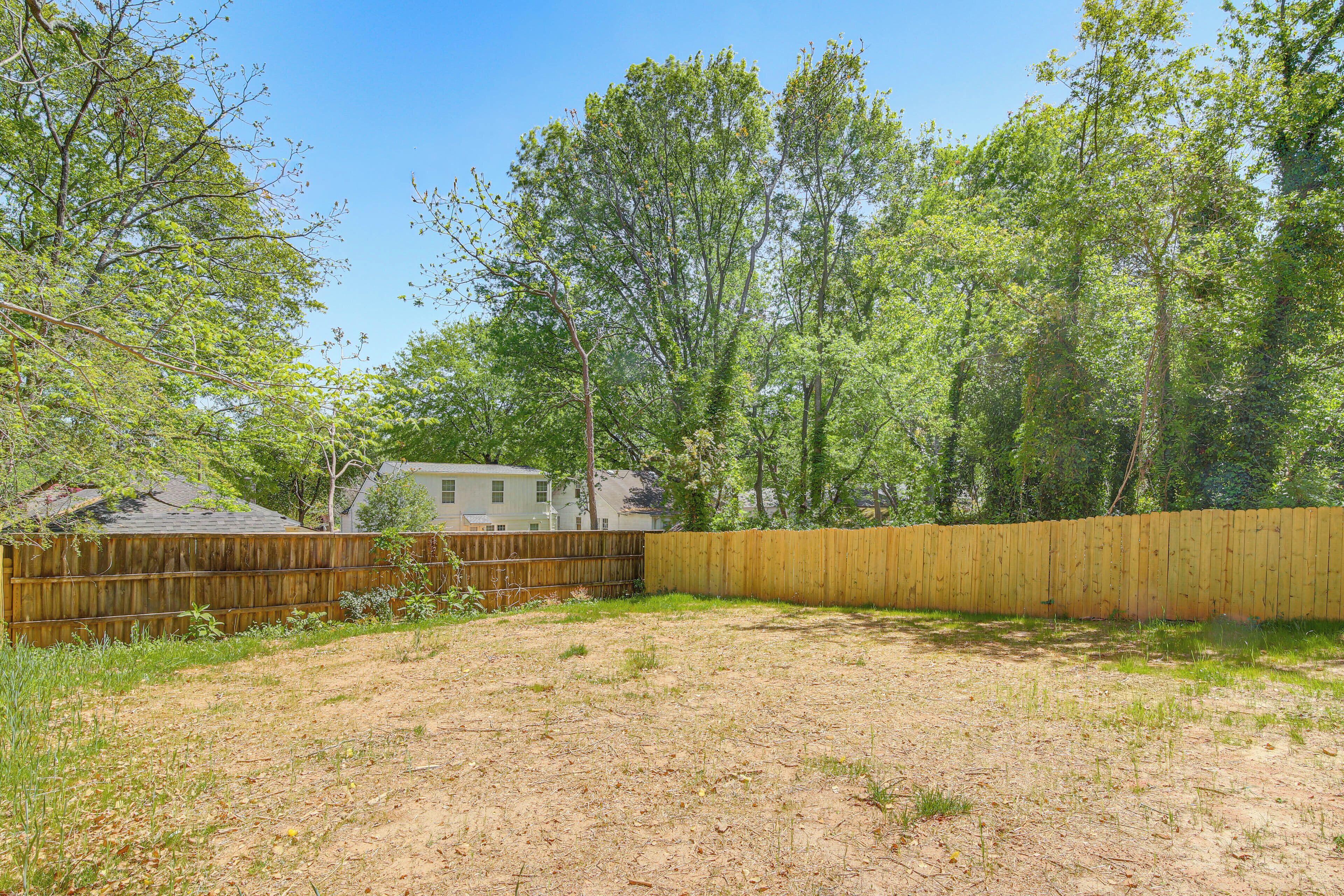 A backyard with a wooden fence, a house in the background, and trees.
