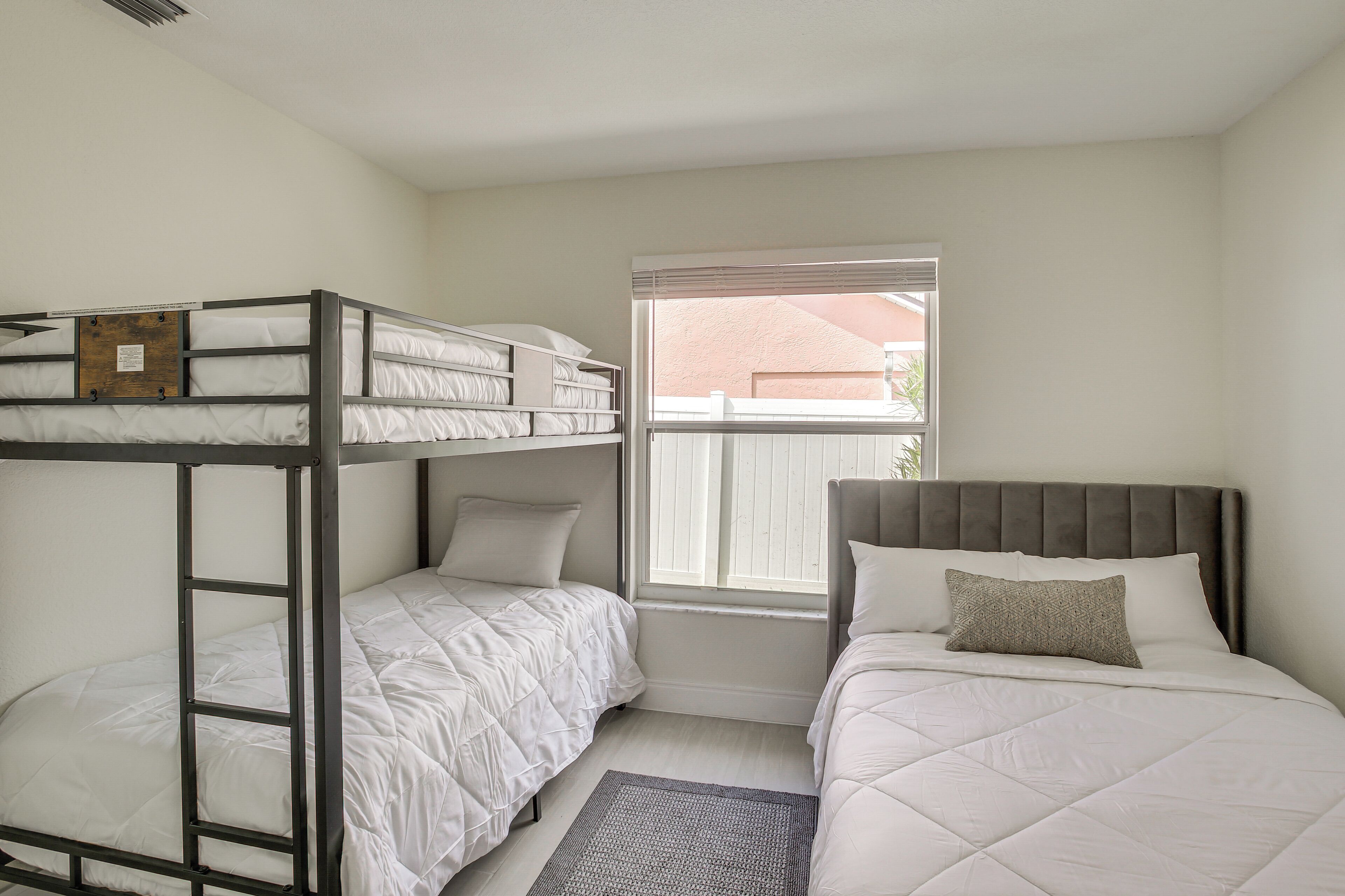 A room with bunk beds, a window with blinds, and a view of the outside.