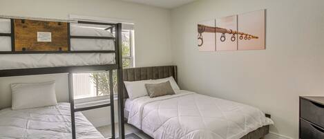Une chambre avec un lit superposé, un lit simple, une tête de lit en bois, un tapis gris et une œuvre d’art accrochée au mur.