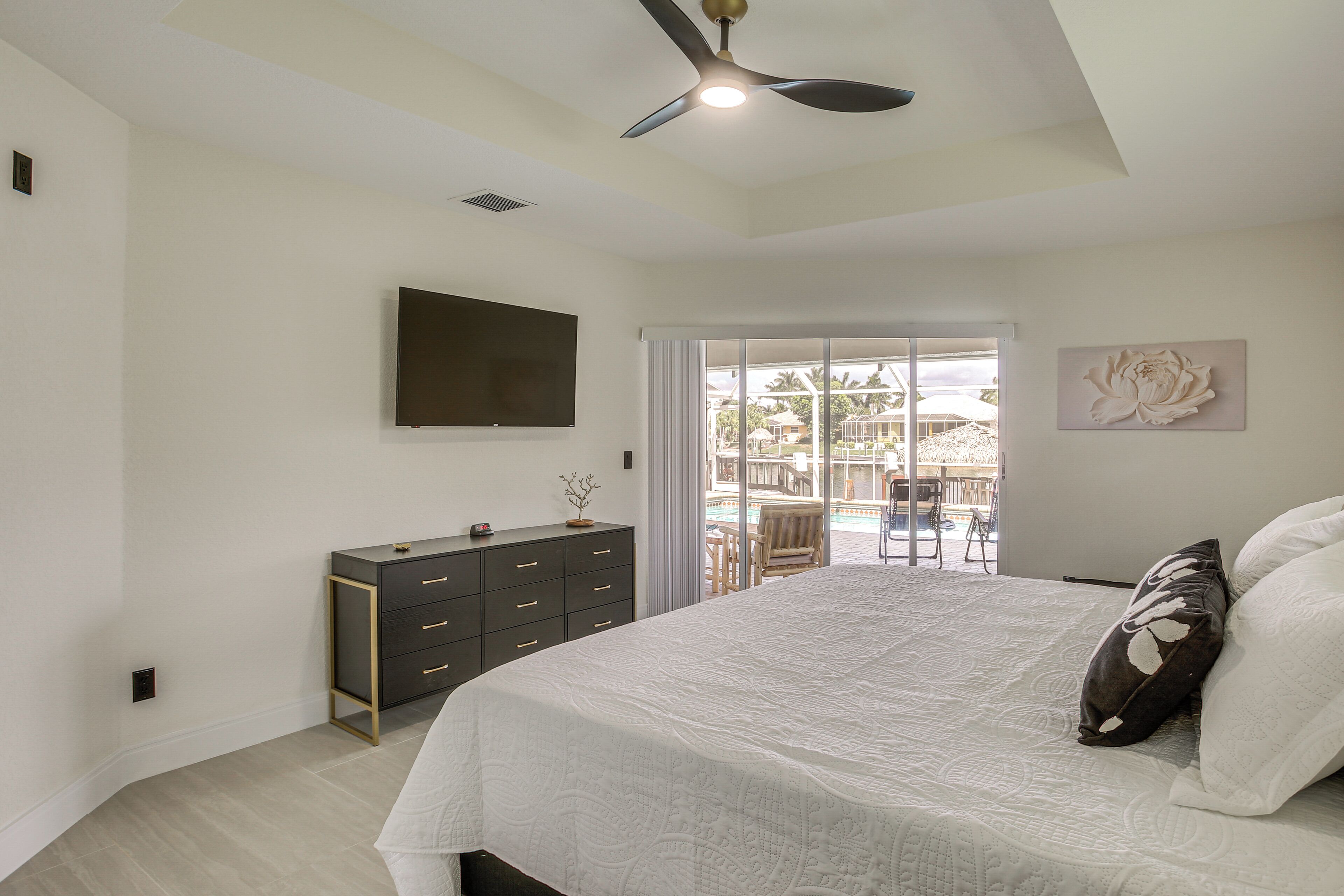 Un dormitorio con cama, cómoda, ventilador de techo, televisor y vista al exterior.