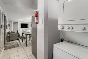 A laundry room with a Whirlpool washer and dryer, a fire extinguisher, a dining area with a table and chairs, and a living area with a sofa and a television. - 1 Mi to Pennekamp State Park! Family Home w/ Patio (Key Largo)