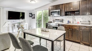 A modern kitchen with dark wooden cabinets, a large microwave, and a dining area with a marble table and grey chairs.