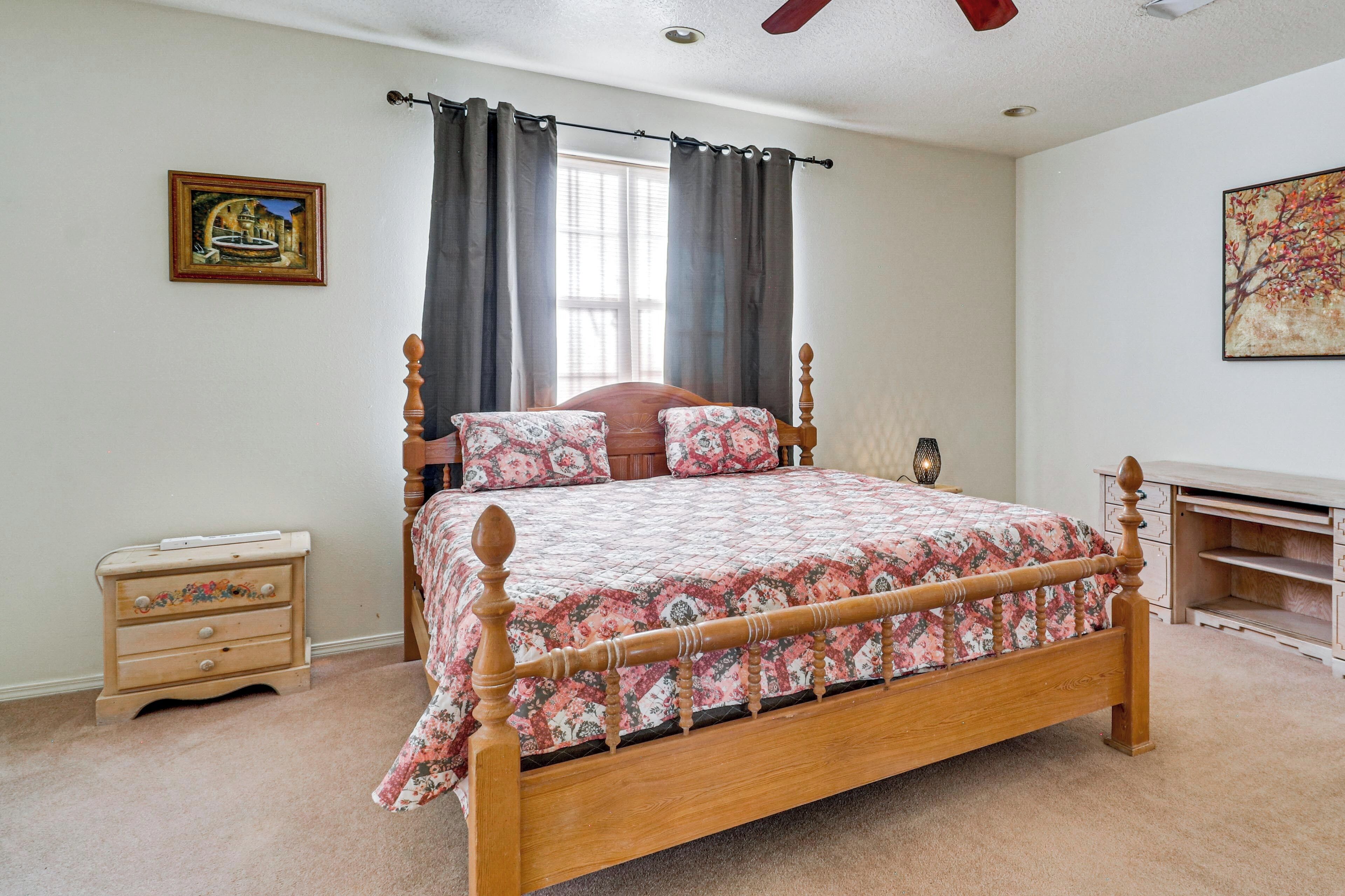 A bedroom with a wooden bed, a nightstand, a dresser, a window with curtains, and a painting on the wall.