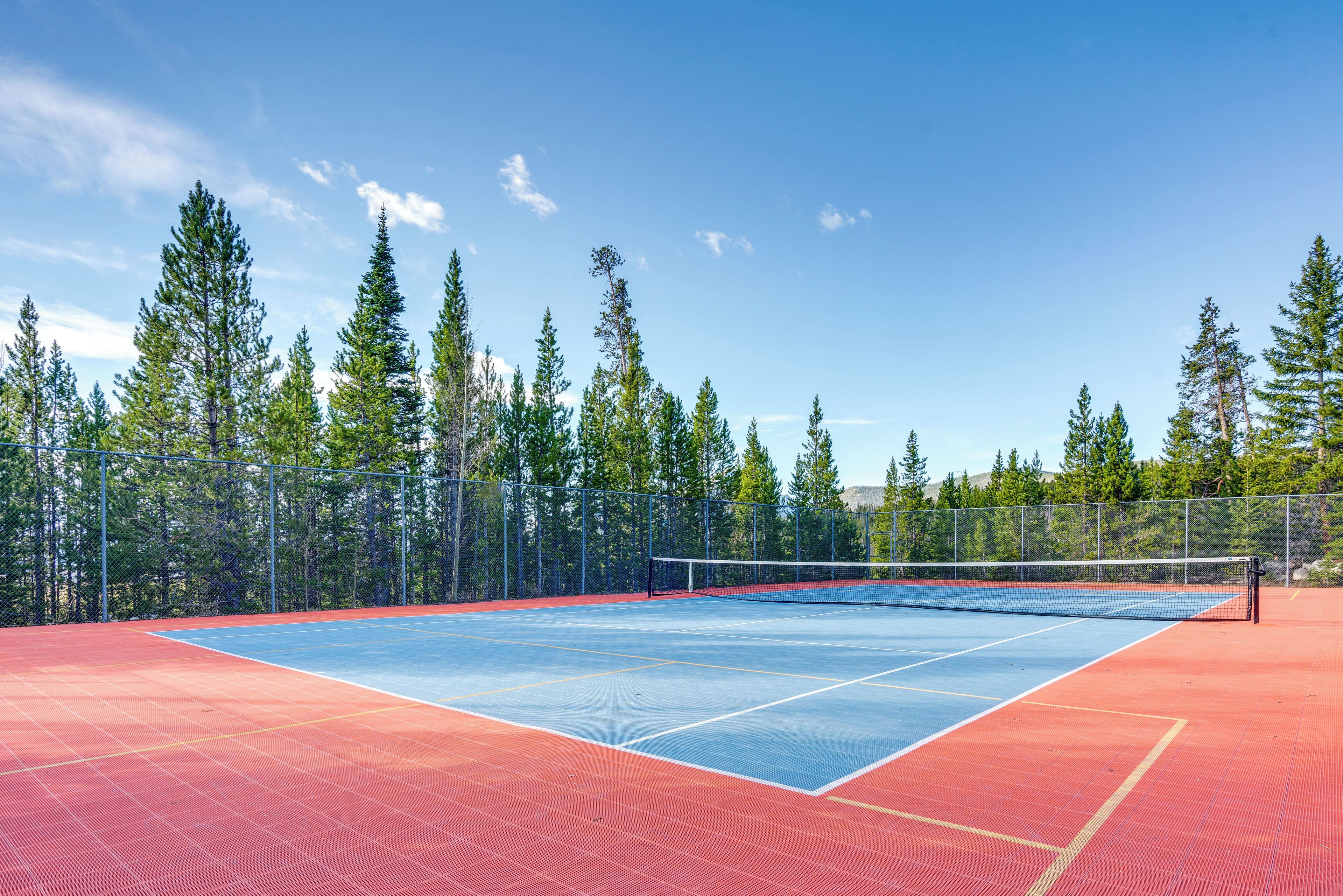 An outdoor tennis court with a net, surrounded by a fence and trees.