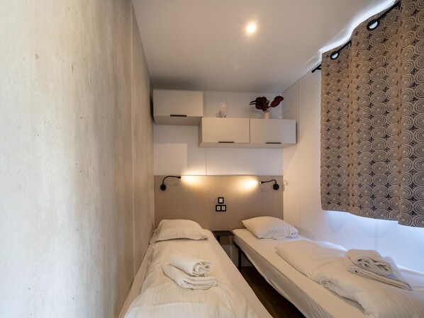 Habitación de hotel con dos camas individuales, una mesita de noche pequeña, un estante en la pared con un jarrón y una cortina estampada.