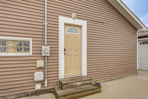 A house with a beige front door, a small set of wooden steps, and a garage door.