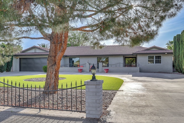 A modern two-story house with a well-maintained lawn, a metal fence, and a driveway leading to the garage.