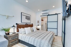 Une chambre à coucher comprenant un lit, une table de chevet, une lampe, des œuvres d’art murales et une plante.