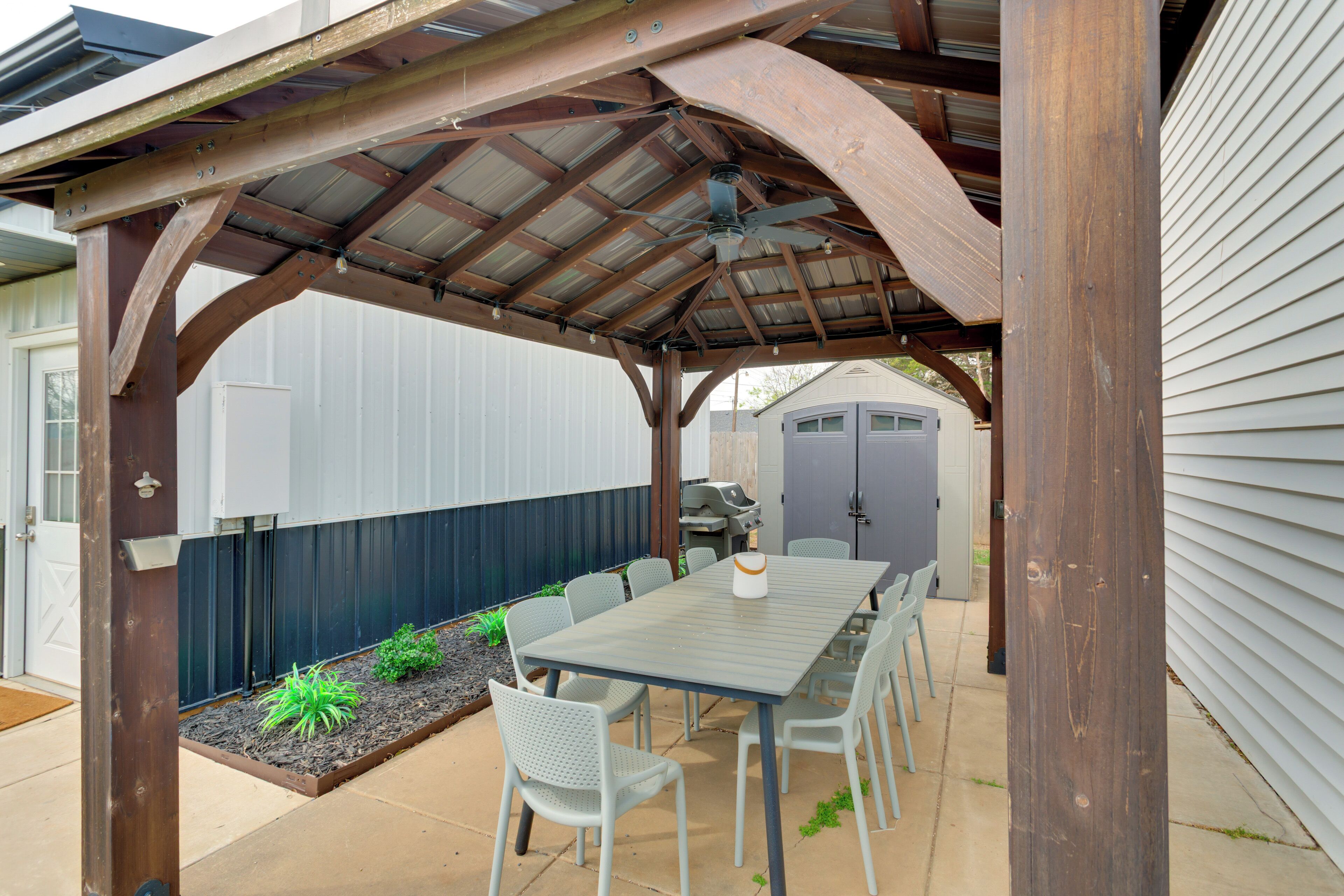 A covered patio with a table and chairs, a ceiling fan, and a grill area.