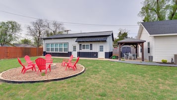 A residential house with a covered patio, a lawn with red chairs, and a wooden fence.