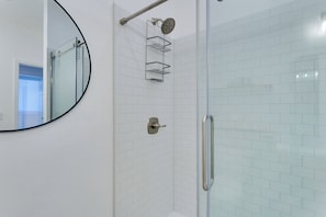 A modern bathroom with a glass shower enclosure, a round mirror, and a metal towel rack. - 1 Mi to OU! Sleek Guest House w/ Gas Grill (Norman)