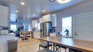 A modern kitchen with white cabinets, a stainless steel refrigerator, and a wooden dining table with benches. - Walk to Norman Hot Spots: Family-friendly Home! (Norman)