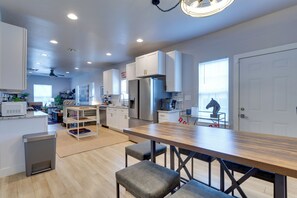 A modern kitchen with white cabinets, a stainless steel refrigerator, and a wooden dining table with benches. - Walk to Norman Hot Spots: Family-friendly Home! (Norman)