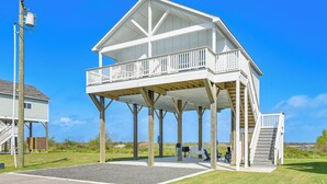 Uma casa de praia de dois andares com varanda, área de estar coberta ao ar livre e escada que dá acesso ao andar superior.