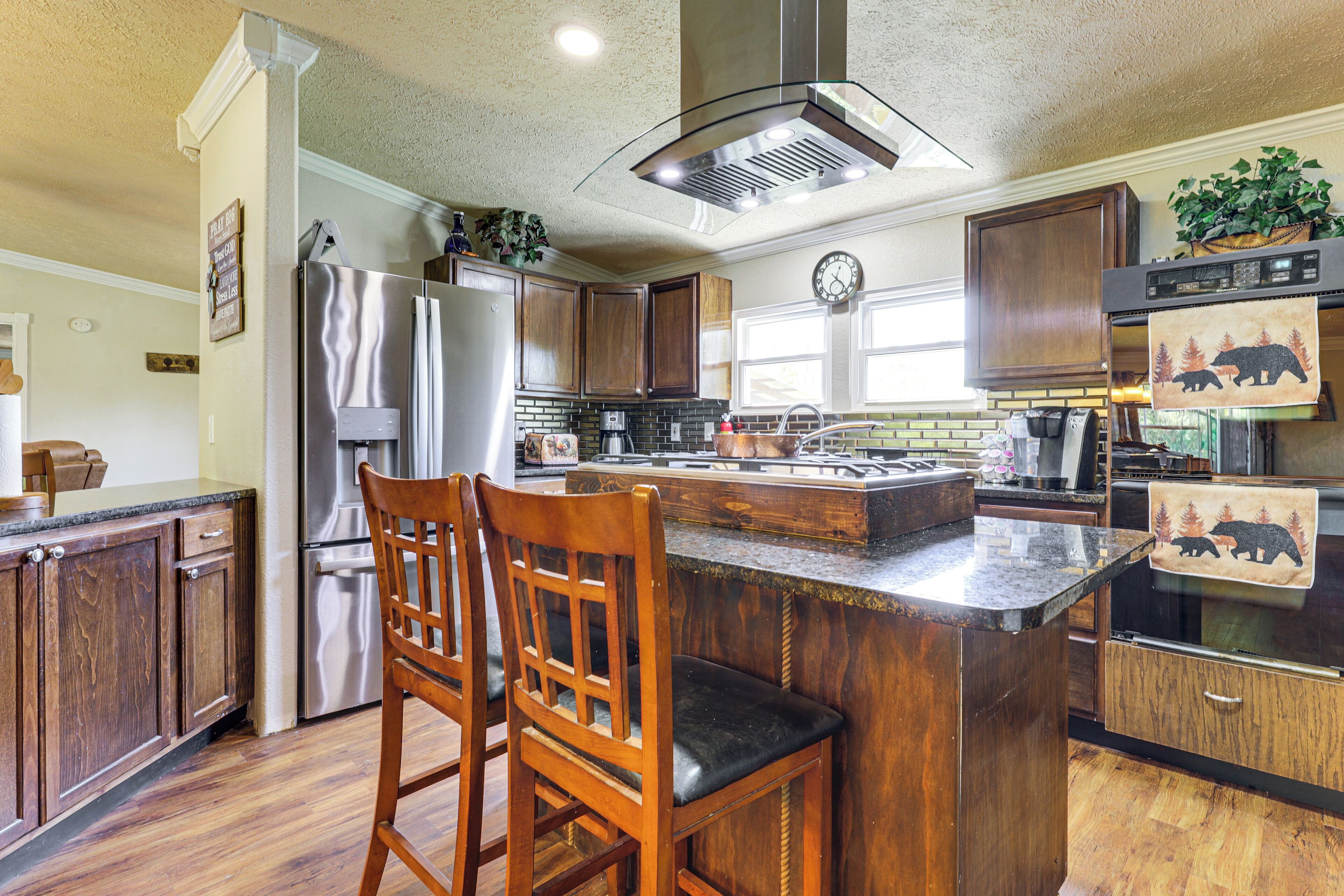 A kitchen with wooden cabinets, a stainless steel refrigerator, a large island with bar stools, and a clock on the wall.