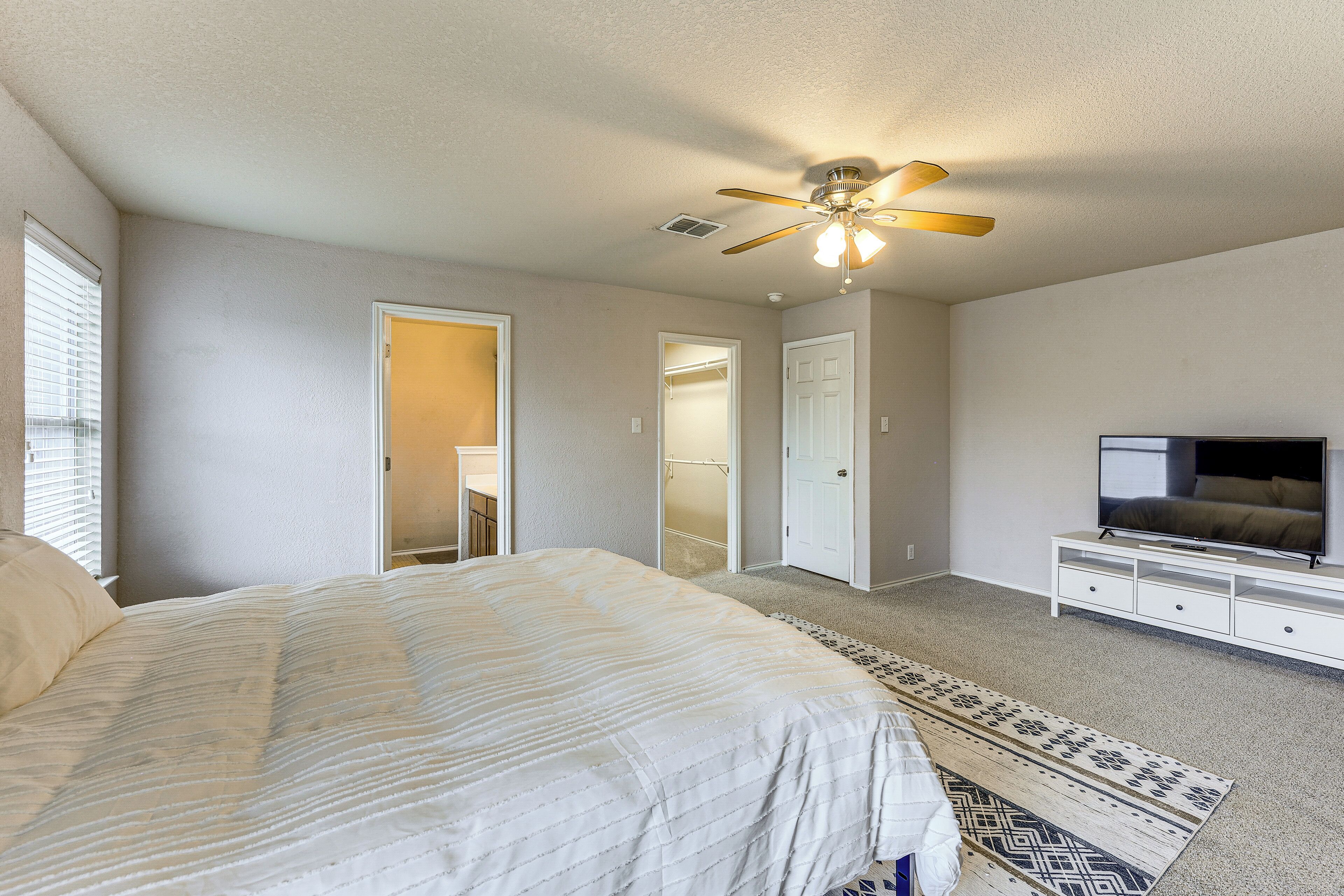 A bedroom with a bed, a ceiling fan, a TV, and a walk-in closet.