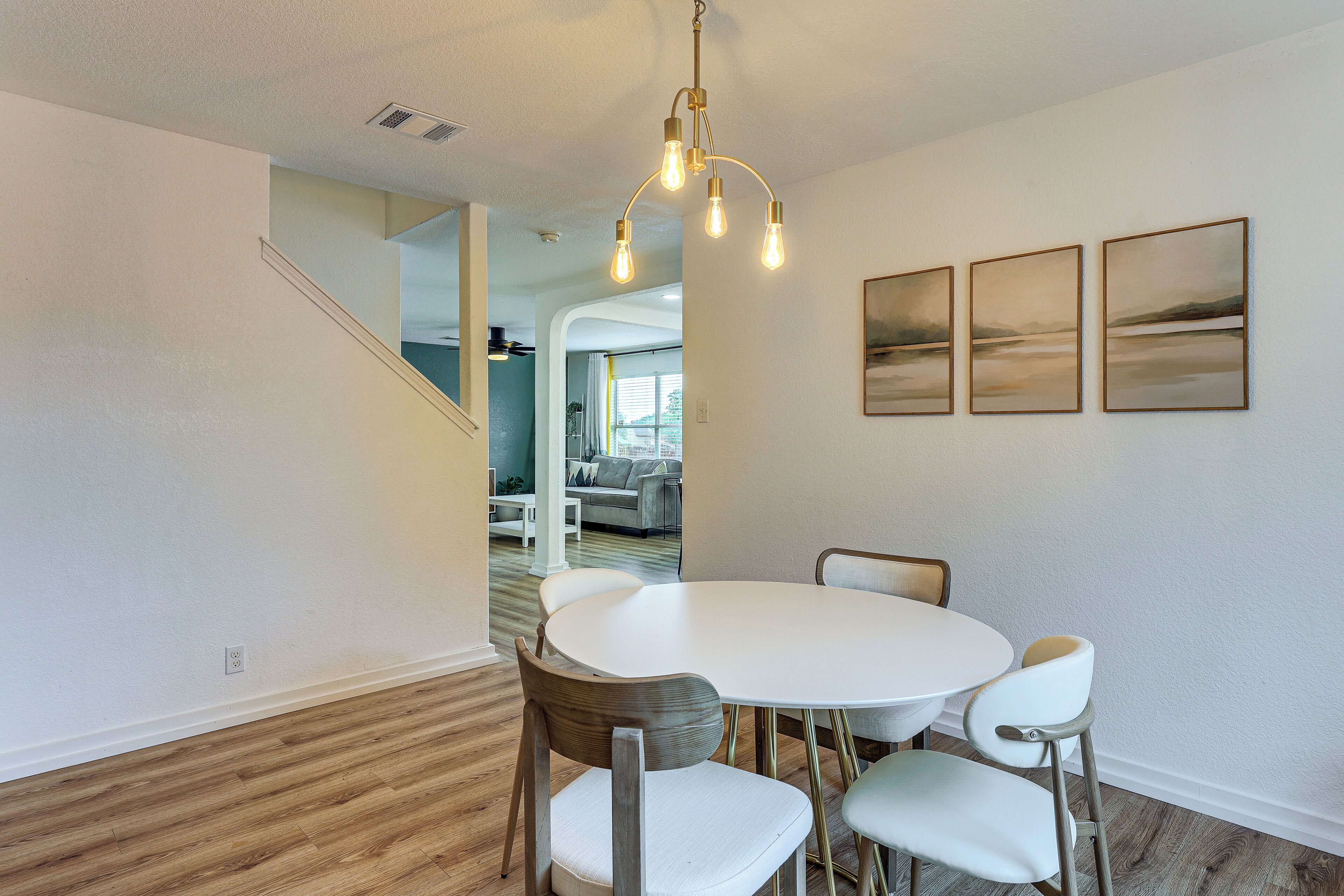 A dining area with a round table and four chairs, a staircase, and three framed artworks on the wall.