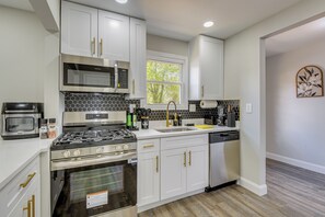 A modern kitchen with white cabinets, stainless steel appliances, and a window providing natural light.