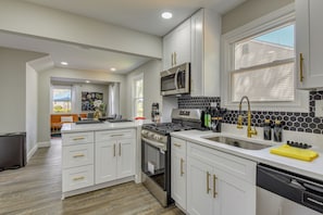 A modern kitchen with white cabinetry, stainless steel appliances, and a large window.