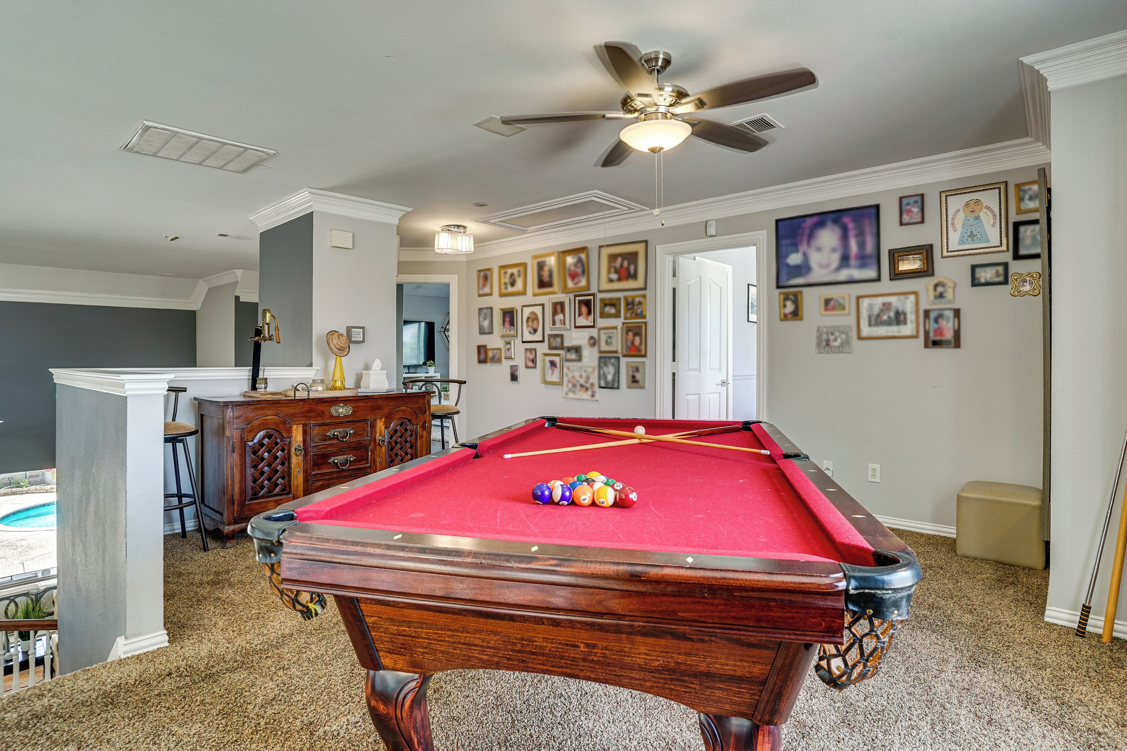A pool table with balls, a ceiling fan, and a wall with framed pictures.