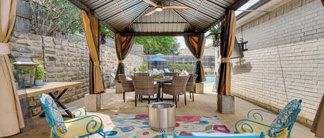 An outdoor patio with a covered seating area, a table, and a ceiling fan.