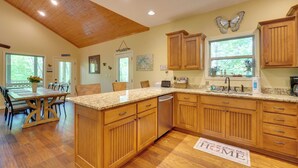 A kitchen with wooden cabinets, a granite countertop, and a dining area with a table and chairs. - 3 Mi to Marina on Dale Hollow Lake! Cabin Getaway (Byrdstown)