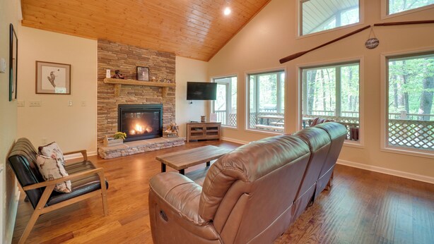 A spacious living room with a fireplace, large windows, a leather sofa, and a wooden ceiling. - 3 Mi to Marina on Dale Hollow Lake! Cabin Getaway (Byrdstown)