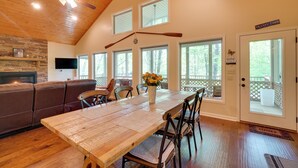 A spacious dining area with a wooden table and chairs, a built-in fireplace, and a large window overlooking a deck. - 3 Mi to Marina on Dale Hollow Lake! Cabin Getaway (Byrdstown)