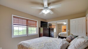 Ein Schlafzimmer mit Bett, Deckenventilator, Kommode, Spiegel und einer Tür zu einem anderen Raum.