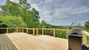 Eine Holzterrasse mit Geländer, mit Blick auf eine bewaldete Landschaft.